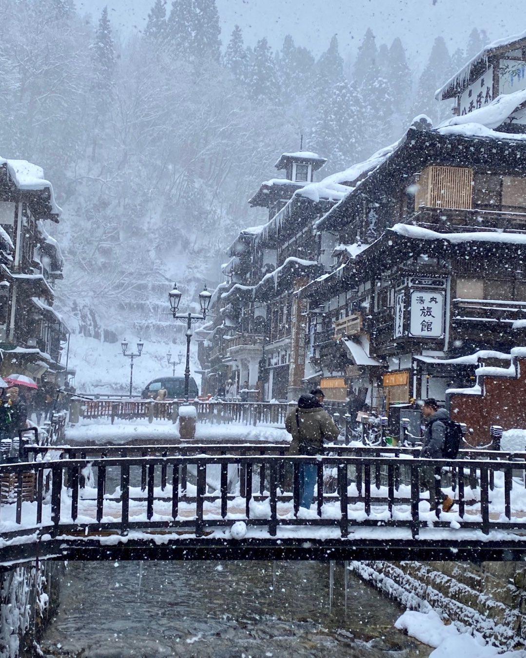 Cities in Japan to see snow - visitors walking on a bridge in Ginzan Onsen
