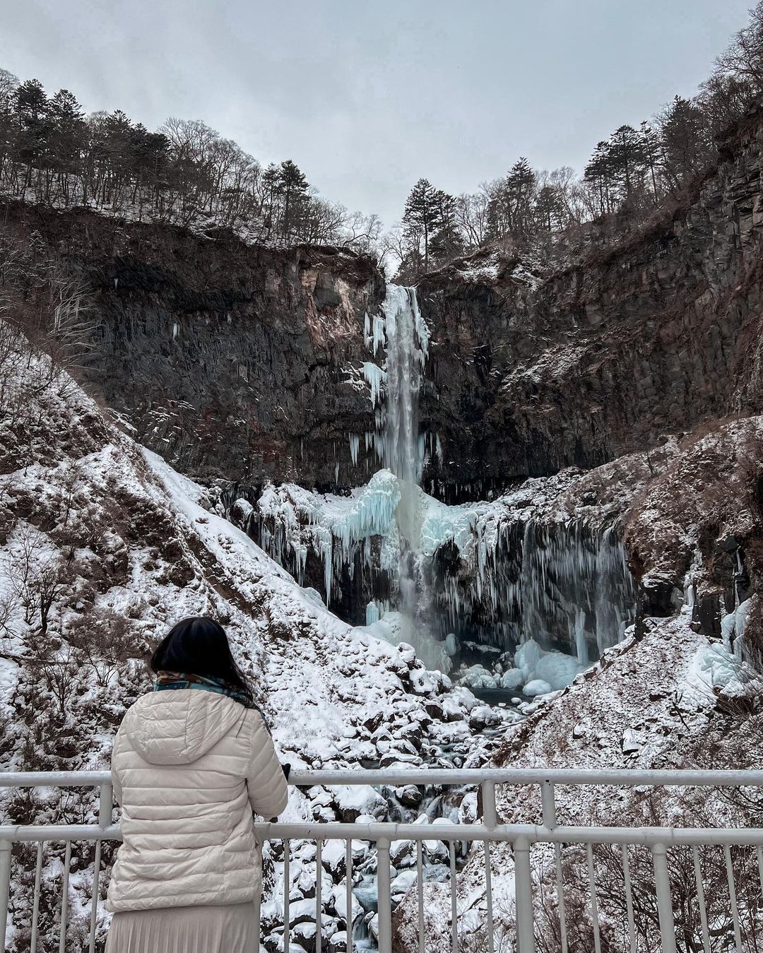 Cities in Japan to see snow - visitor staring at the frozen Kegon Waterfall